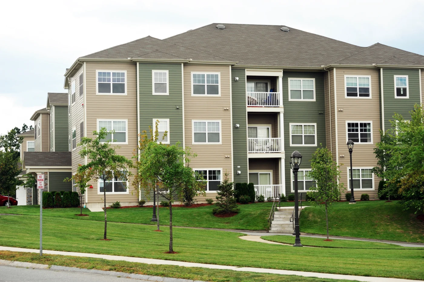 An apartment building with beige and green siding, white trim, and a shingle roof.