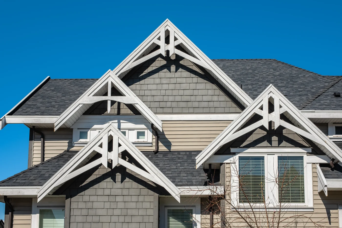 A home with tan and gray siding, white trim, and a gray shingle roof.