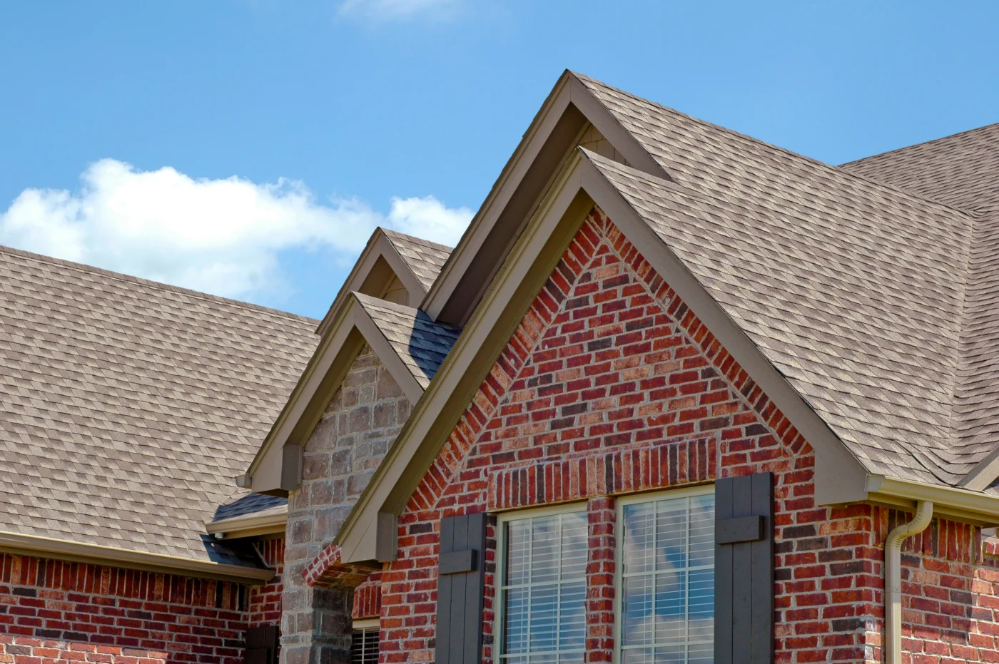A red brick home with a brown shingle roof.