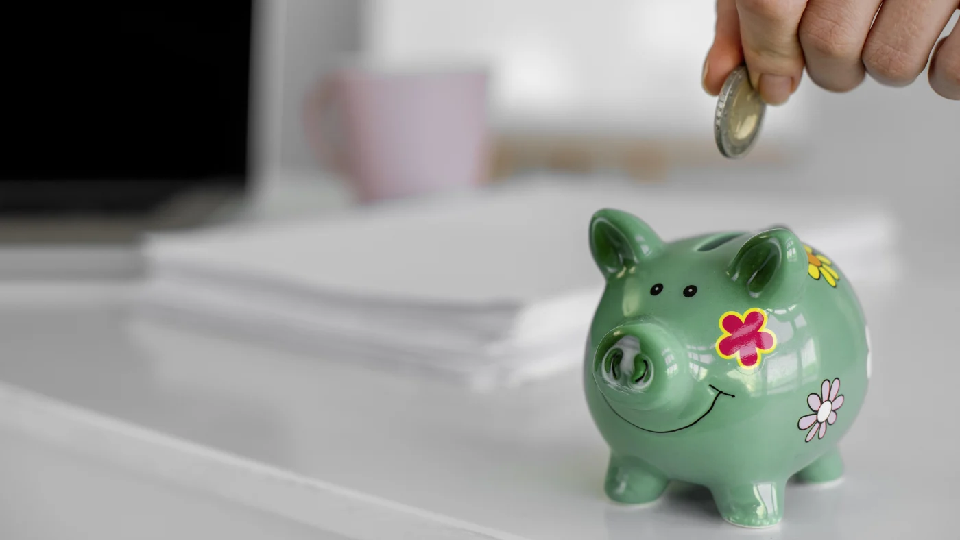 A hand adds a coin to a green piggy bank