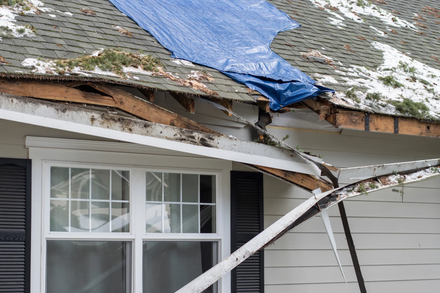 A damaged roof partially covered with a tarp.