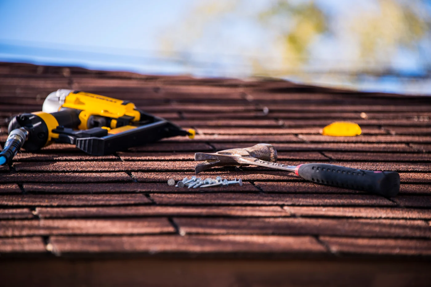 A roofer’s tools rest on a shingle roof