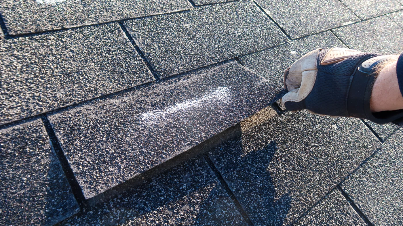 A roofer inspects a damaged shingle on a home.
