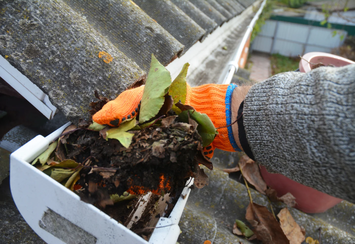 A contractor with an orange glove pulls debris from a gutter.