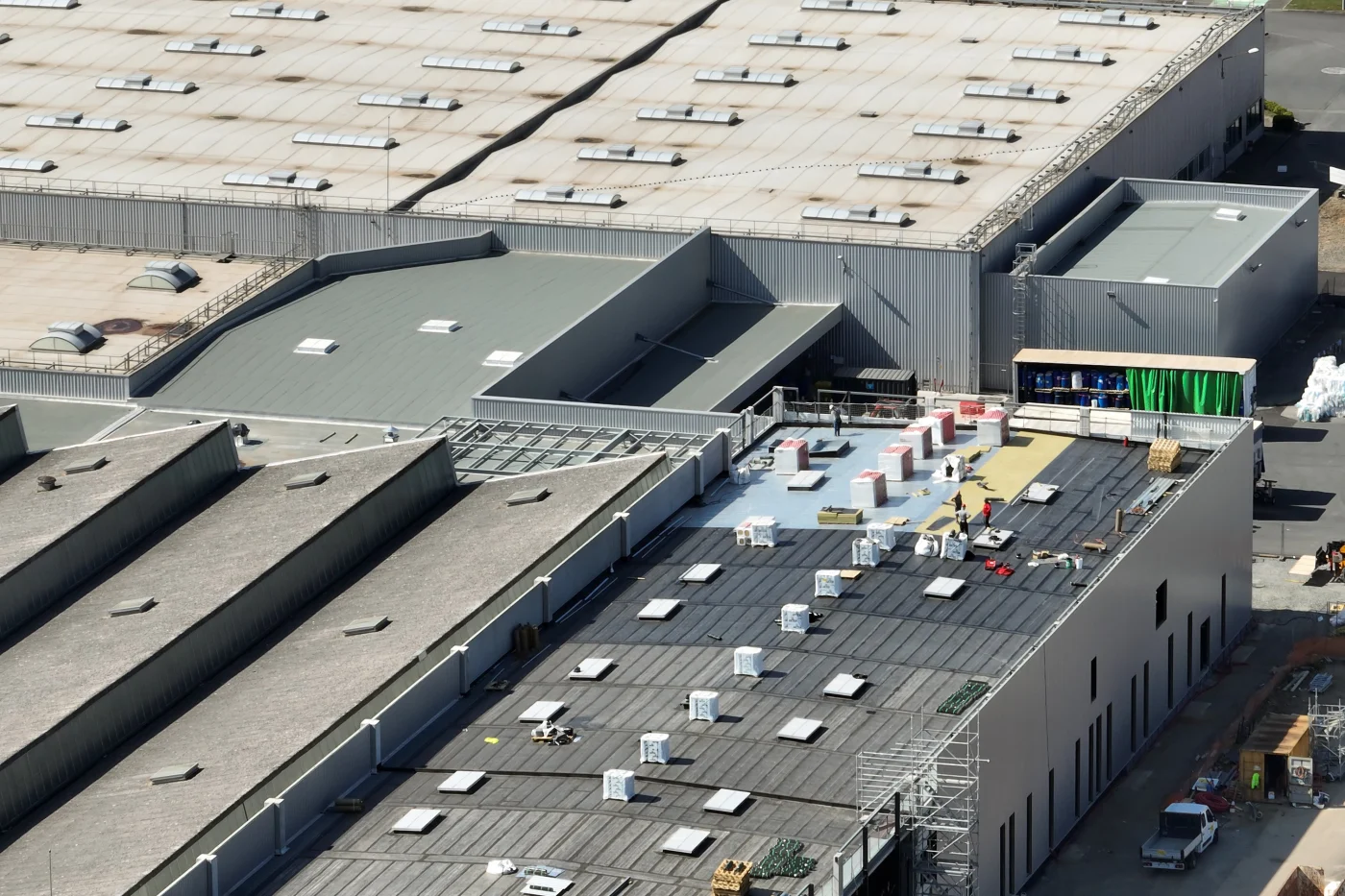 A large commercial building with multiple flat and sloped rooftops, where construction workers are installing roofing materials