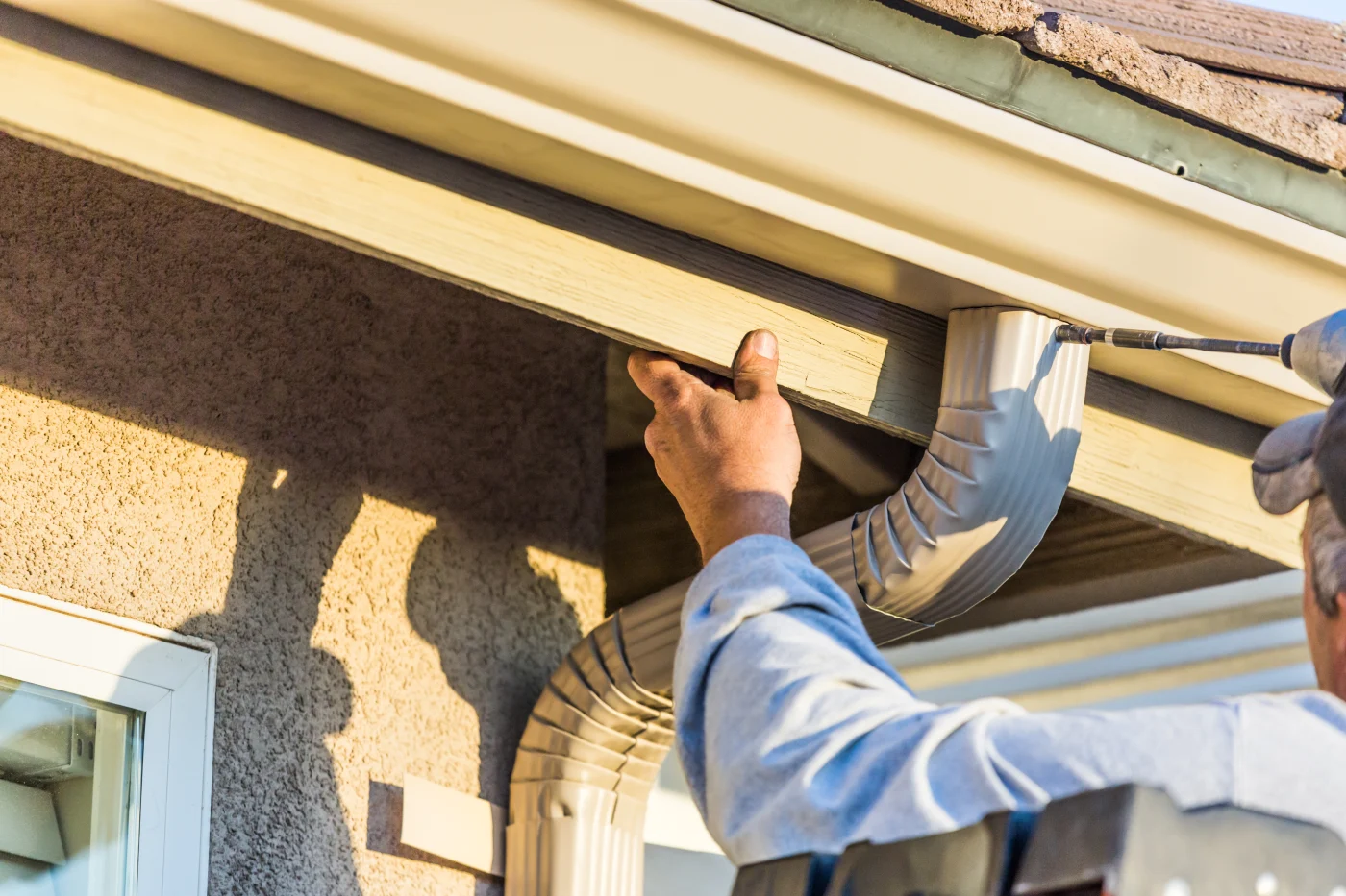 Worker Attaching Aluminum Rain Gutter And Down Spout To Fascia Of House.