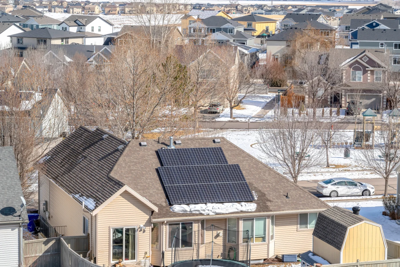 Residential neighborhood in Thornton, CO, during winter, featuring a beige single-story home with solar panels on the roof and light snow.