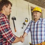 A construction professional wearing a hard hat shakes hands with a homeowner, representing trust, integrity, and strong working relationships.