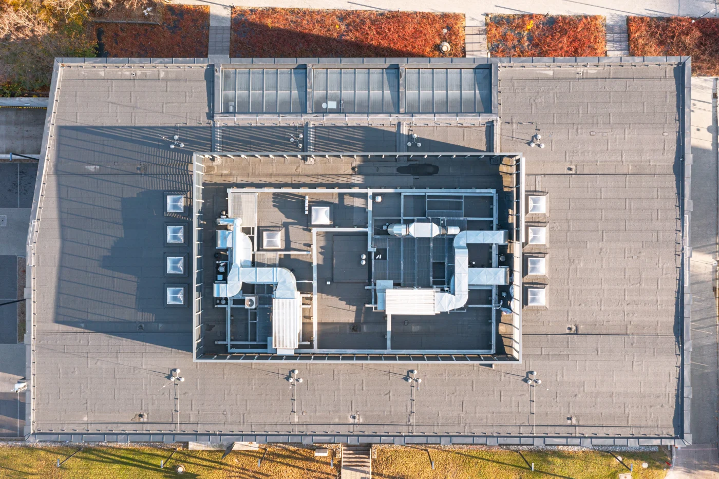 Wide aerial view of a large commercial flat roof with HVAC units, vents, conduit lines, and a yellow metal perimeter, showing typical industrial rooftop equipment