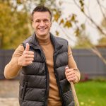 A smiling homeowner gives a thumbs-up while holding a shovel in a backyard, symbolizing satisfaction and confidence.