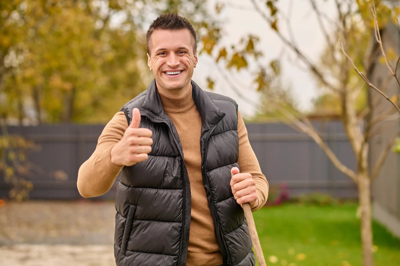 A smiling homeowner gives a thumbs-up while holding a shovel in a backyard, symbolizing satisfaction and confidence.