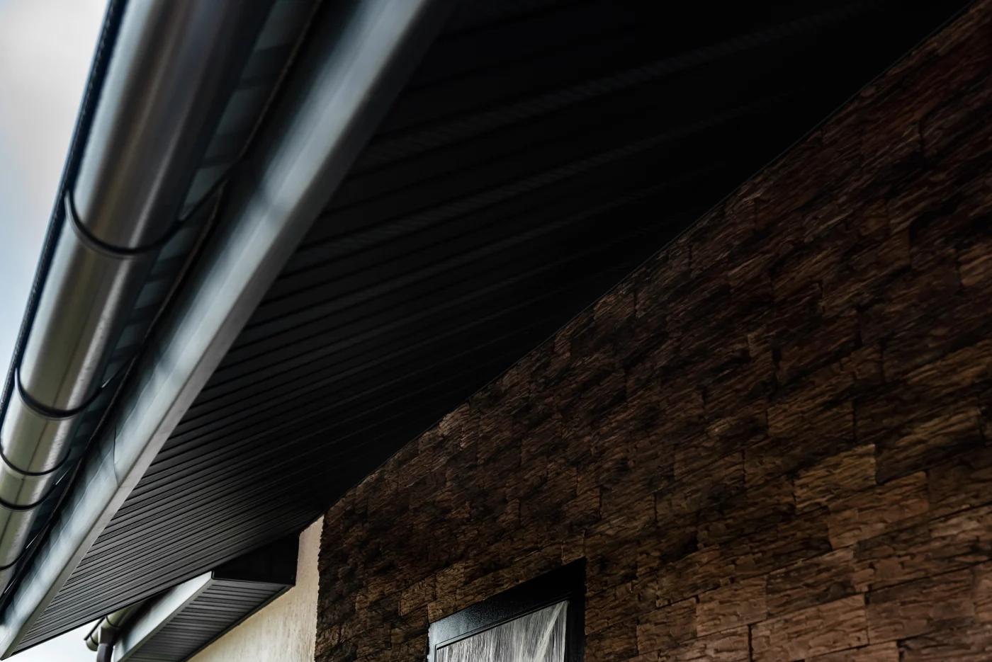 Close-up of a modern building’s dark metal gutter and soffit running along a textured stone exterior wall