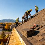A roofing crew installing asphalt shingles on a residential roof with safety harnesses, tools, and mountain views in the background.