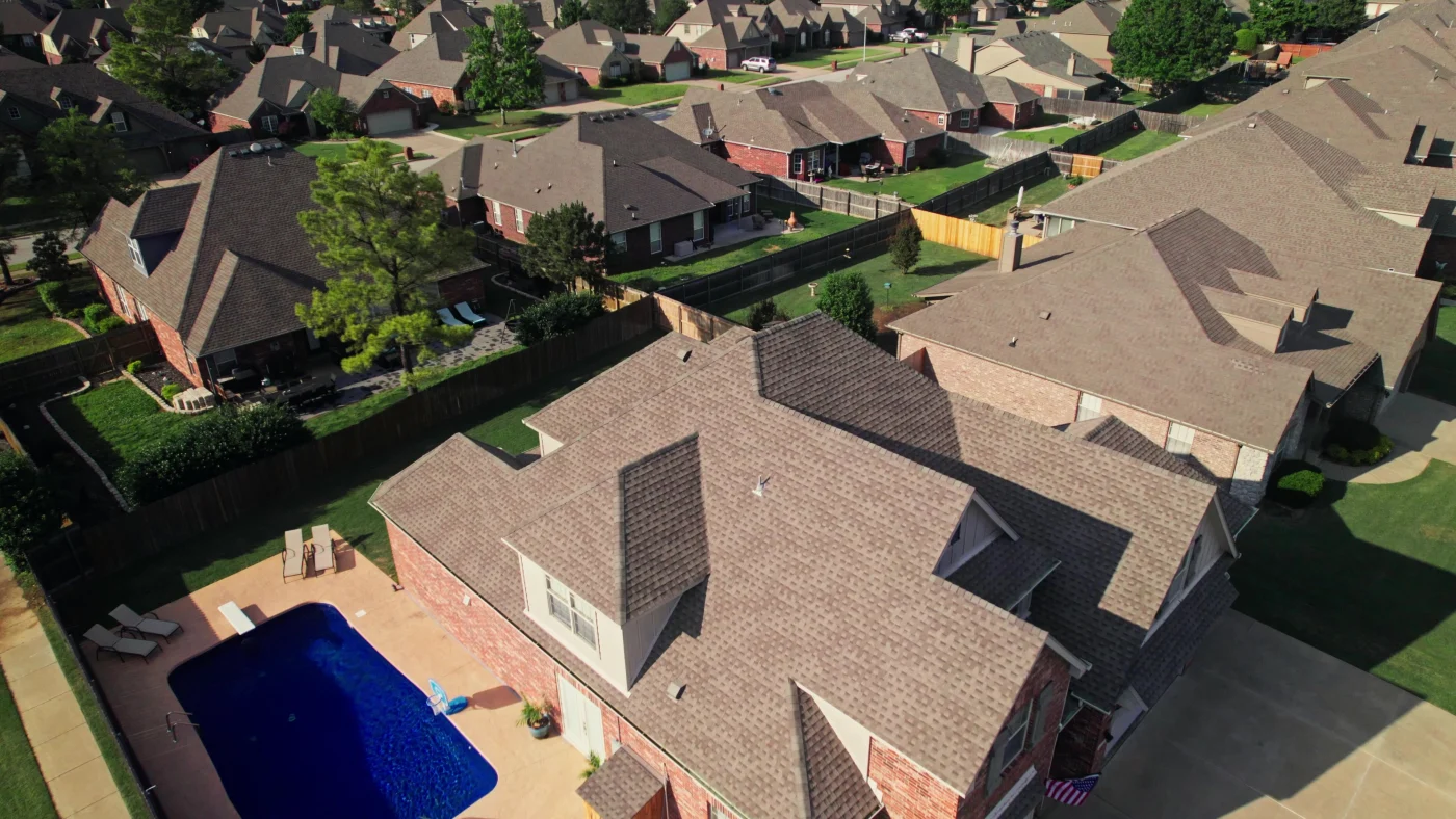 Aerial view of a suburban neighborhood with shingle roofs, fenced yards, green lawns, and a backyard swimming pool.